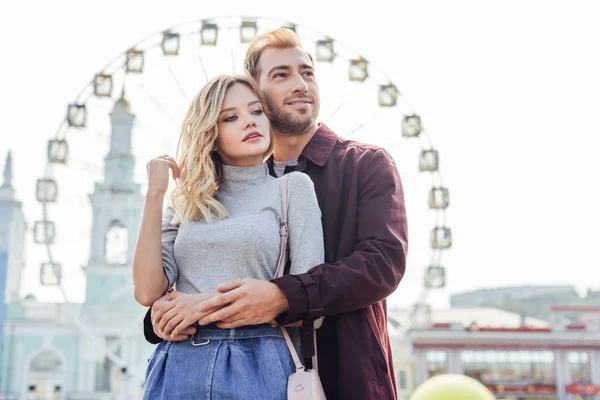 Stylish couple in autumn outfit cuddling with observation wheel on background — Stock Photo