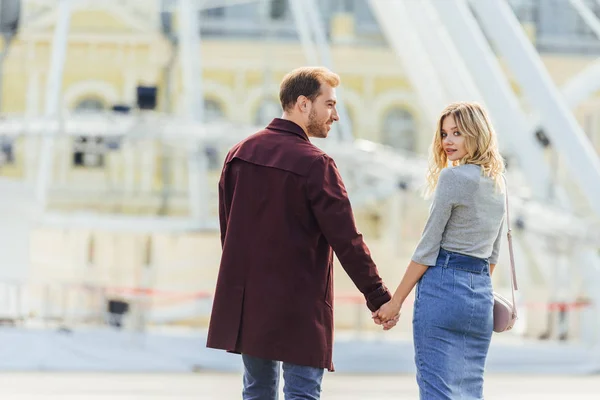 Rear view of couple in autumn outfit holding hands and walking in city — Stock Photo