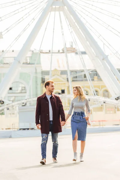 Couple en tenue d'automne tenant la main et marchant près de la roue d'observation — Photo de stock