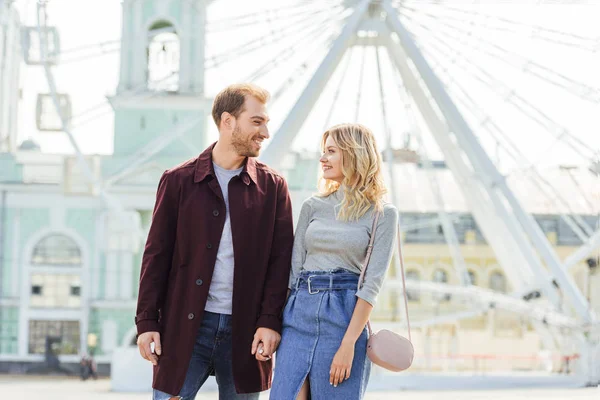 Pareja en traje de otoño tomados de la mano y mirándose el uno al otro cerca del volante de observación - foto de stock