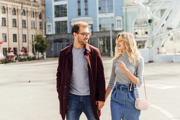 Усміхнена пара в осінньому вбранні тримає руки і дивиться один на одного в місті — стокове фото