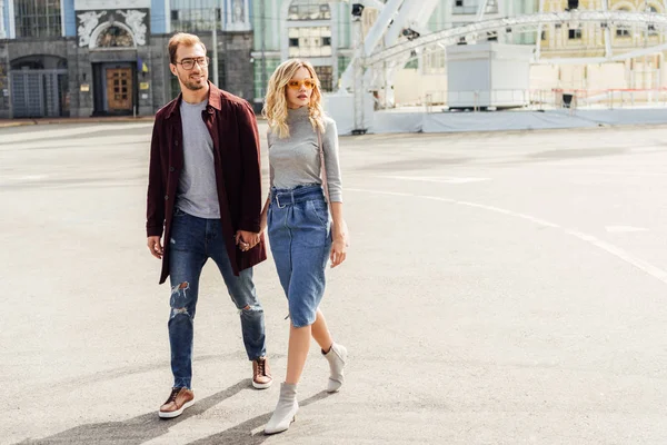 Pareja con estilo en traje de otoño tomados de la mano y caminando juntos en la ciudad - foto de stock