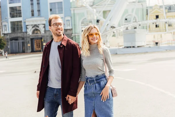 Sonriente pareja romántica en otoño traje cogido de la mano y caminando en la ciudad - foto de stock