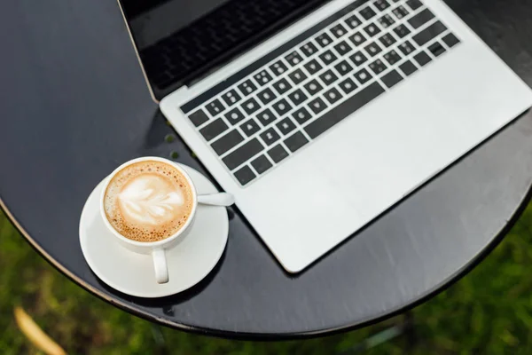 Alto angolo di vista del computer portatile e una tazza di caffè sul tavolo in giardino — Foto stock