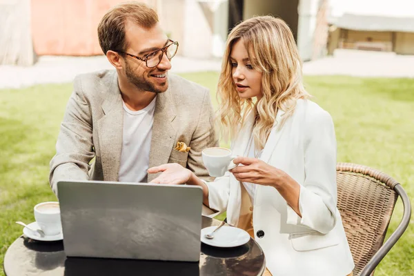 Casal em roupa de outono sentado à mesa com laptop e beber café no café — Fotografia de Stock