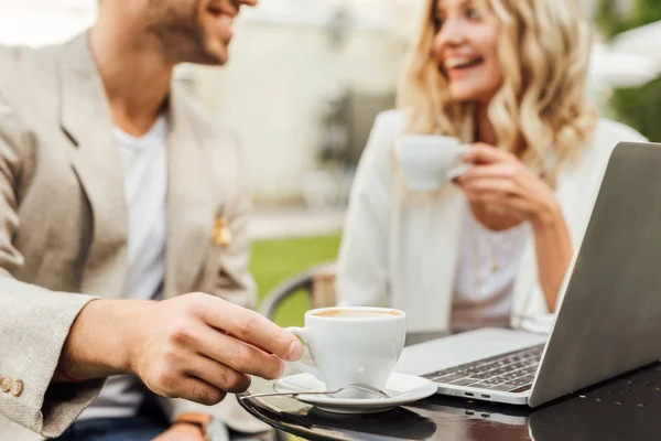 Imagem cortada de casal em roupa de outono sentado à mesa com laptop e beber café no café — Fotografia de Stock
