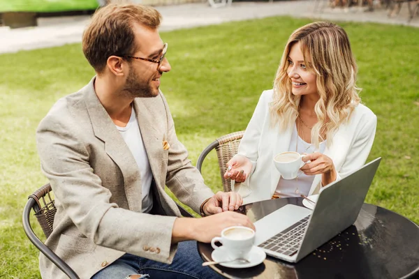 Couple souriant en tenue d'automne assis à table avec ordinateur portable et boire du café dans le café — Photo de stock