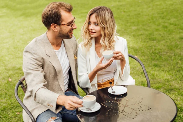 Pareja de arquitectura en traje de otoño sentado en la mesa en la cafetería con café y mirándose el uno al otro — Stock Photo