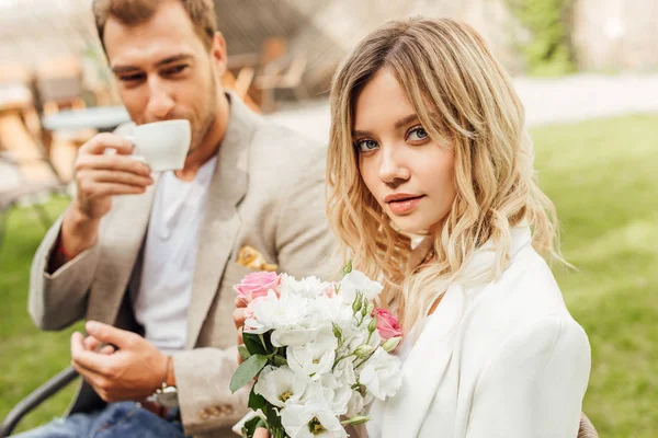Attraente fidanzata tenendo bouquet di rose in caffè, fidanzato bere caffè — Foto stock