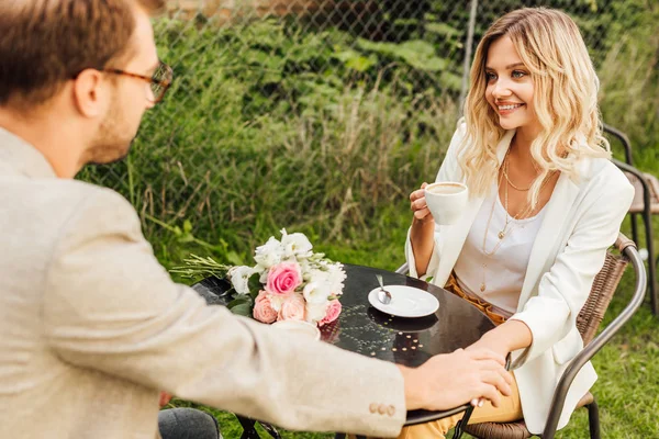 Pareja sonriente en traje de otoño sentado en la mesa en la cafetería y tomados de la mano - foto de stock