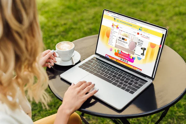 Cropped image of woman using laptop with loaded aliexpress page on table in garden — Stock Photo