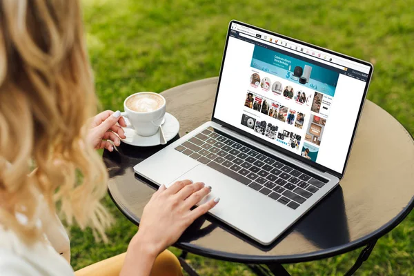 Cropped image of woman using laptop with loaded amazon page on table in garden — Stock Photo