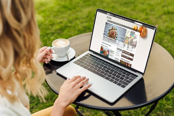 Immagine ritagliata di donna utilizzando computer portatile con caricamento bbc cibo pagina sul tavolo in giardino — Foto stock