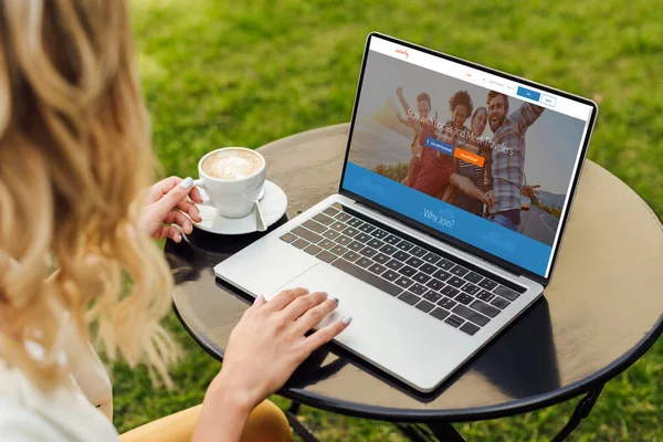 Imagen recortada de la mujer usando el ordenador portátil con página de couchsurfing cargado en la mesa en el jardín — Stock Photo