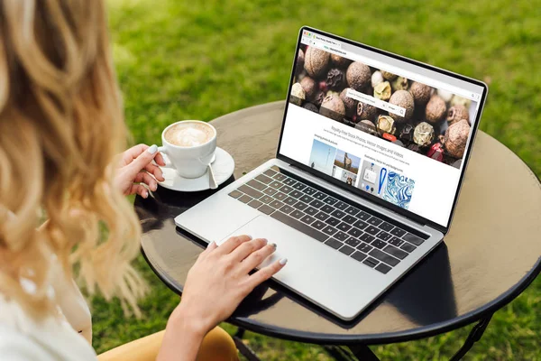 Cropped image of woman using laptop with loaded depositphotos page on table in garden — Stock Photo
