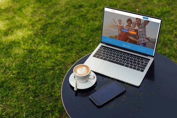 Laptop with loaded couchsurfing page on table in garden — Stock Photo