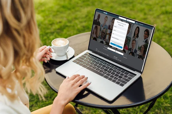 Cropped image of woman using laptop with loaded linkedin page on table in garden — Stock Photo