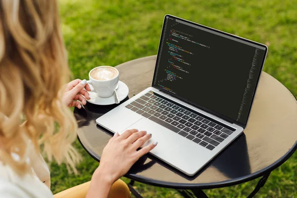 Обітнутого зображення жінки, використовуючи ноутбук з html-коду на столі в саду — стокове фото