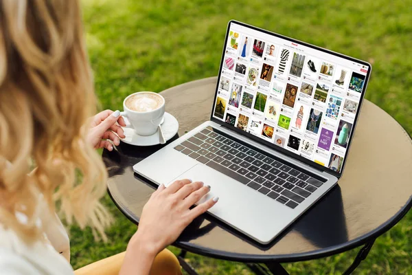 Image recadrée de la femme en utilisant un ordinateur portable avec la page chargée de pinterest sur la table dans le jardin — Photo de stock