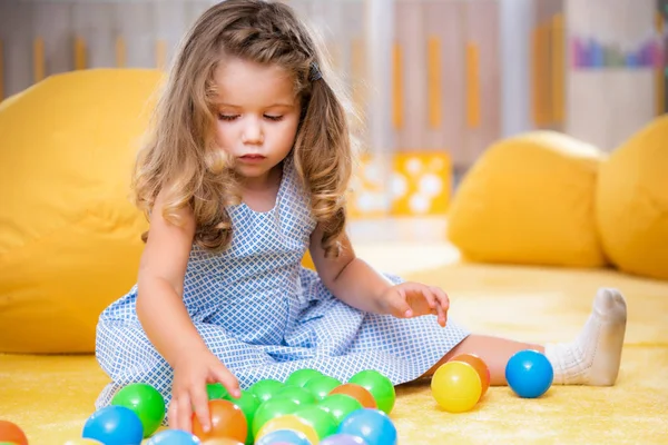 Adorable niño caucásico sentado en la alfombra y jugando con bolas de colores en el jardín de infantes - foto de stock