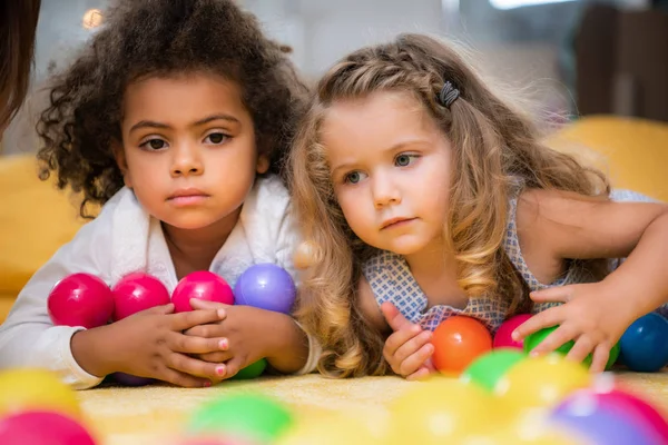 Очаровательные мультикультурные дети, лежащие с красочными мячами в детском саду — стоковое фото