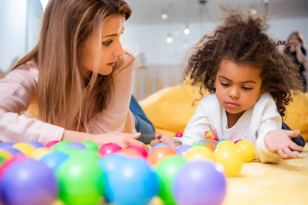Caucasian tutor and adorable african american kid playing with balls in kindergarten — Stock Photo