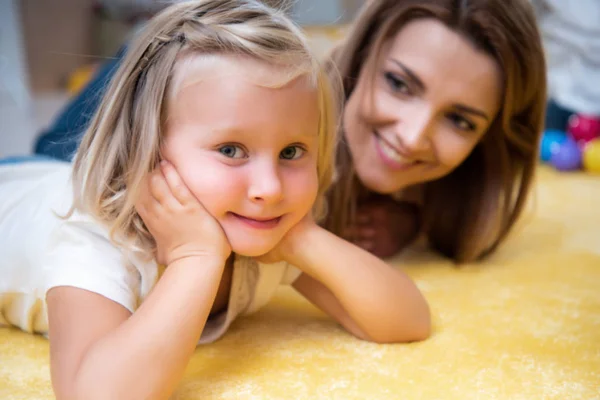 Tuteur souriant regardant adorable enfant reposant menton sur les mains et regardant caméra à la maternelle — Photo de stock
