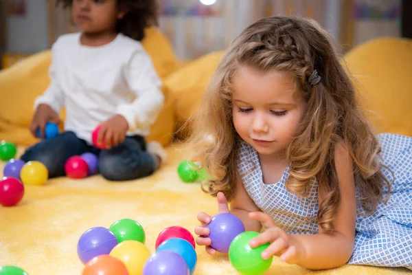 Crianças multiculturais brincando com bolas coloridas no tapete no jardim de infância — Fotografia de Stock