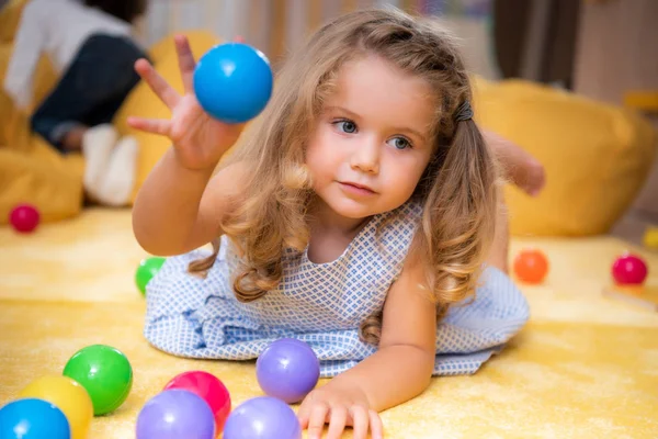 Adorable niño caucásico jugando en la alfombra con bolas de colores en el jardín de infantes - foto de stock