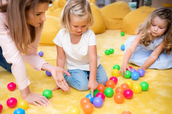 Erzieher gestikuliert auf bunten Bällen zu Kindern im Kindergarten, Kind zeigt auf eine — Stockfoto