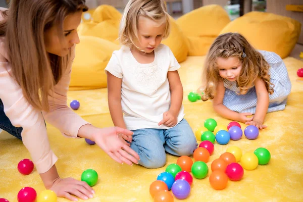 Educador apuntando en bolas de colores a los niños en el jardín de infantes - foto de stock
