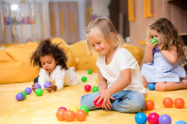 Чарівні мультикультурні діти грають з кольоровими кульками на підлозі в дитячому саду — стокове фото