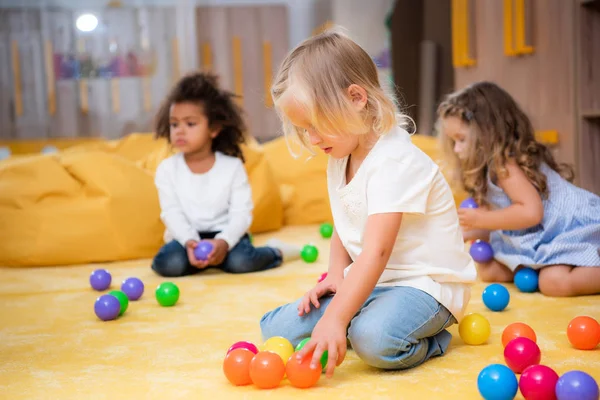 Adorável crianças multiétnicas brincando com bolas coloridas no chão no jardim de infância — Fotografia de Stock