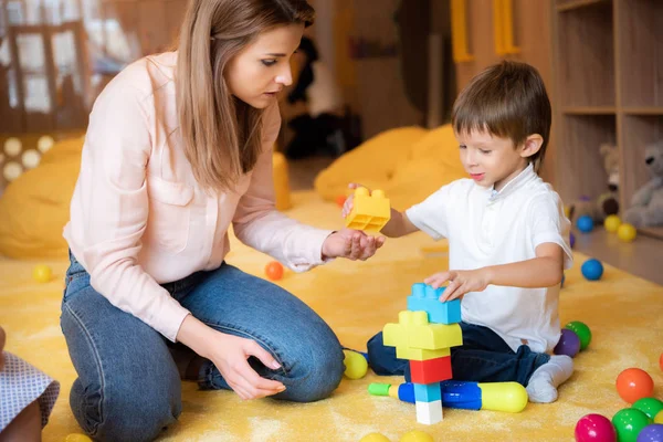Educador y adorable niño jugando con constructor en el jardín de infantes - foto de stock