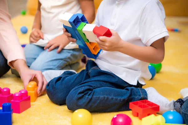 Image recadrée du tuteur et des enfants jouant avec le constructeur à la maternelle — Photo de stock