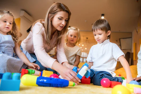 Educador ayudando a los niños a jugar con el constructor en el jardín de infantes - foto de stock