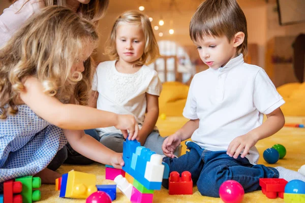 Entzückende Kinder spielen mit Bauarbeiter auf dem Fußboden im Kindergarten — Stockfoto