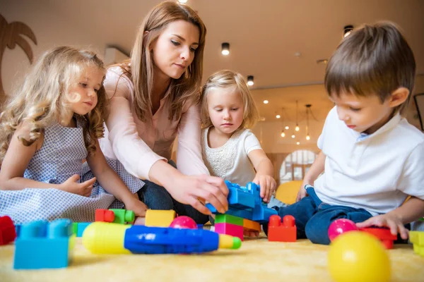 Educator and adorable kids playing with constructor in kindergarten — Stock Photo