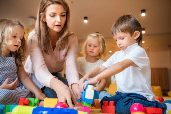 Erzieher und Kinder spielen im Kindergarten mit farbigem Plastikbaukasten — Stockfoto