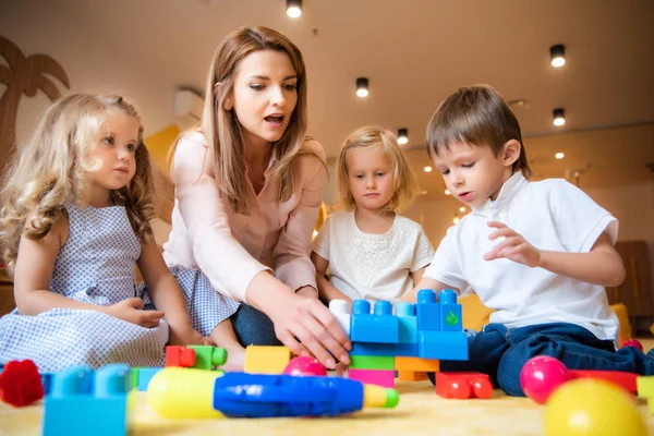 Caucasian educator helping kids playing with constructor in kindergarten — Stock Photo