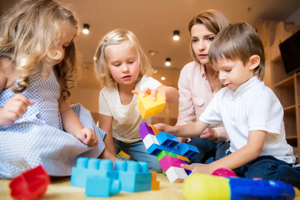 Nivel de superficie del tutor y los niños que juegan con el constructor en el jardín de infantes - foto de stock