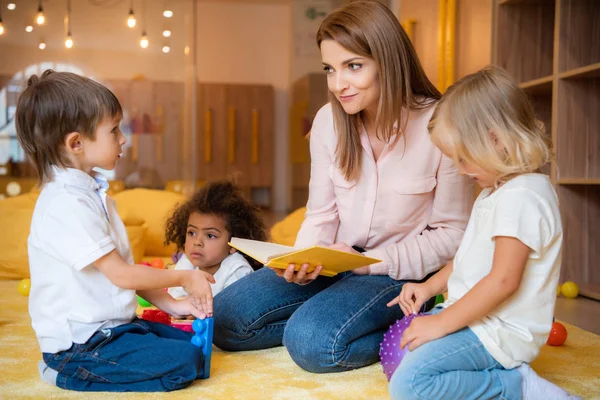 Pädagogin liest Buch für multikulturelle Kinder im Kindergarten — Stockfoto