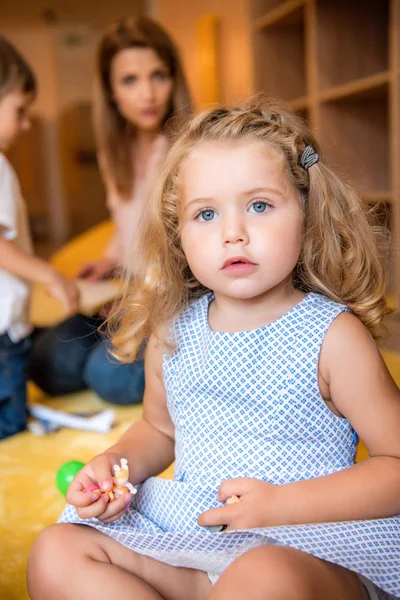 Criança adorável segurando pequenos brinquedos e olhando para a câmera no jardim de infância — Fotografia de Stock