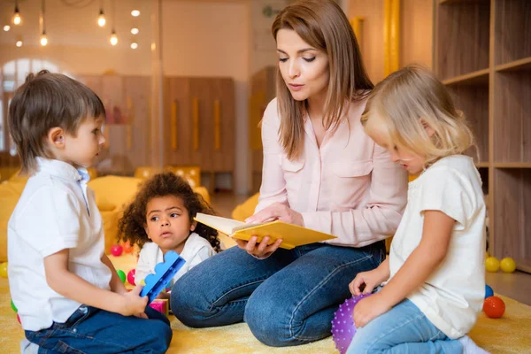 Libro di lettura tutor per adorabili bambini multiculturali nella scuola materna — Foto stock