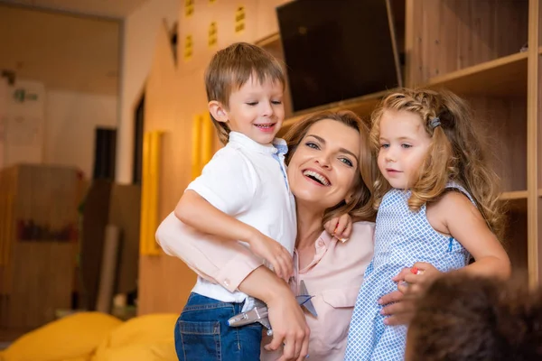 Happy educator hugging adorable smiling kids in kindergarten — Stock Photo