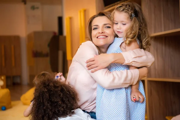 Усміхнений педагог обнімає чарівну дитину в дитячому садку — стокове фото