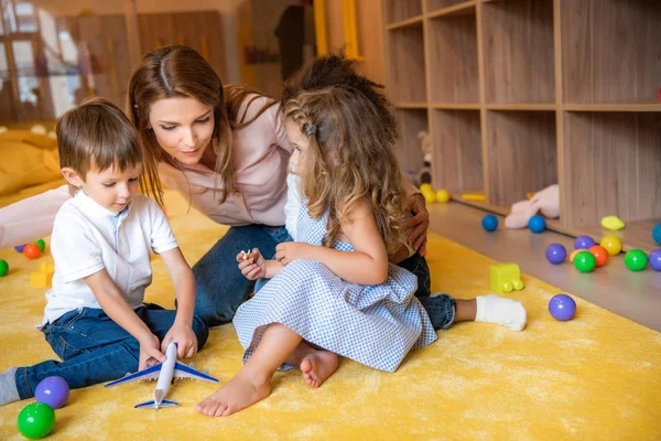 Tutor hugging adorable kids on carpet in kindergarten — Stock Photo