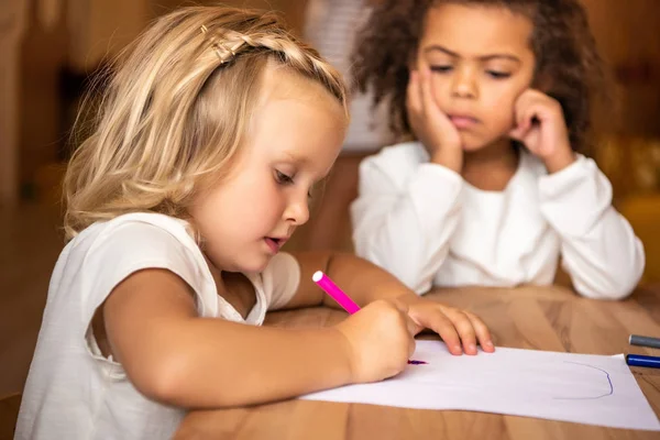 Afro-américain enfant regardant caucasien enfant dessin à la table dans la maternelle — Photo de stock