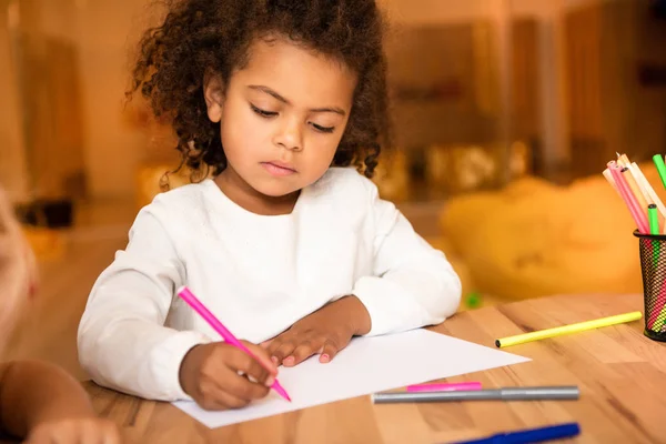 Adorable africano americano niño dibujo con rosa fieltro pluma en el jardín de infantes - foto de stock