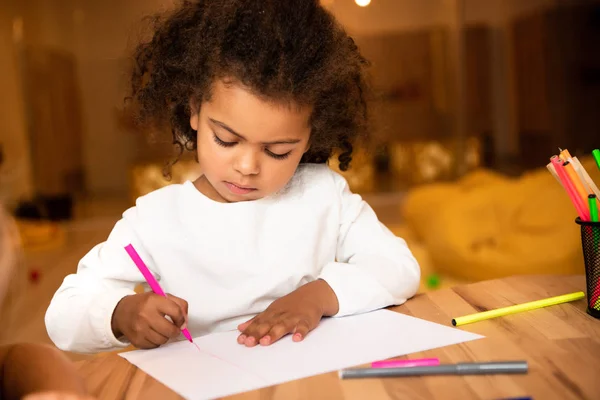 Adorable african american child drawing with pink felt pen in kindergarten — Stock Photo